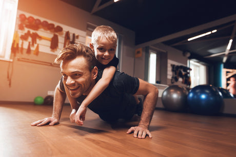 father does pushup with son on back in gym