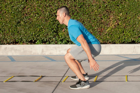 man in a squat using prosourcefit agility ladder during agility drills